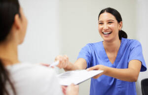 Friendly medical assistant handing clipboard with documents to patient
