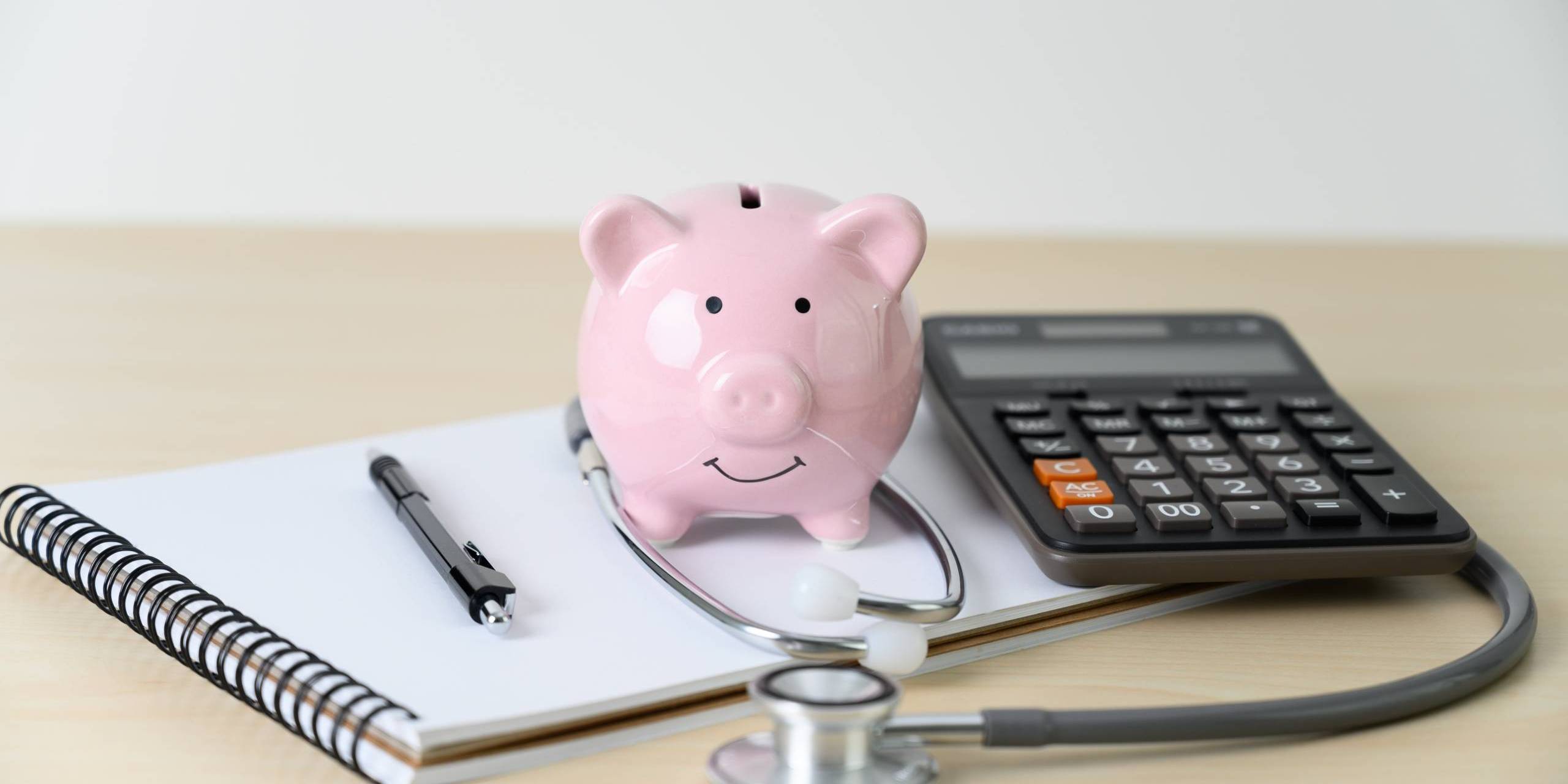 piggy bank on medical items and notebook piggy bank on a notebook with pen and stethoscope