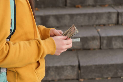 Teenage girl counts dollar bills on the background of the stairs counting money for finances