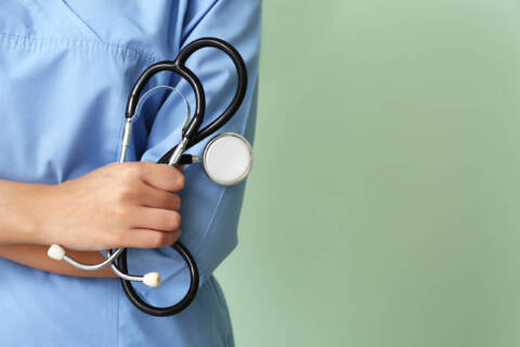 how to fix the nursing shortage Young nurse with stethoscope on color background, closeup
