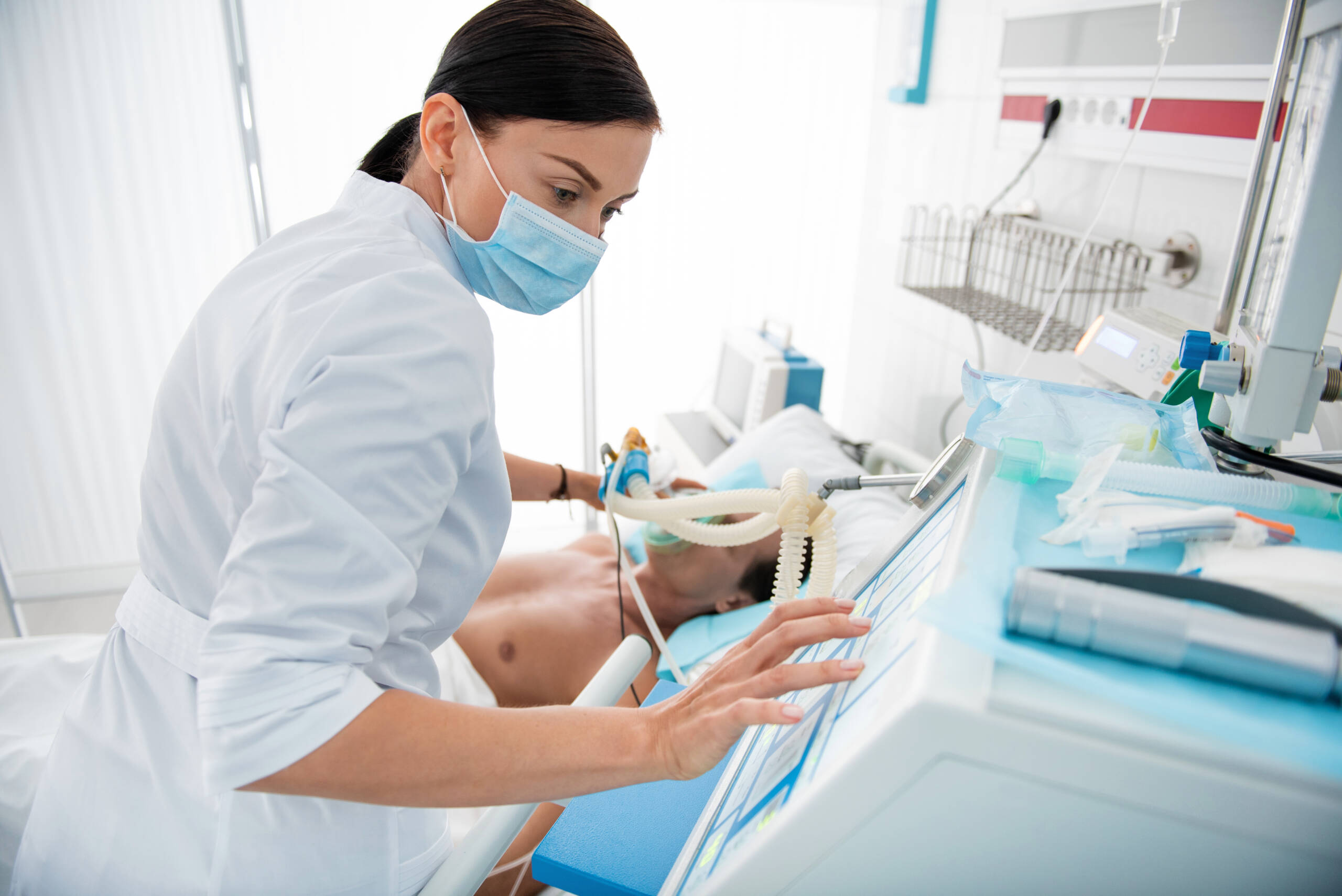 Young doctor checking breathing machine while putting oxygen mask on patient
