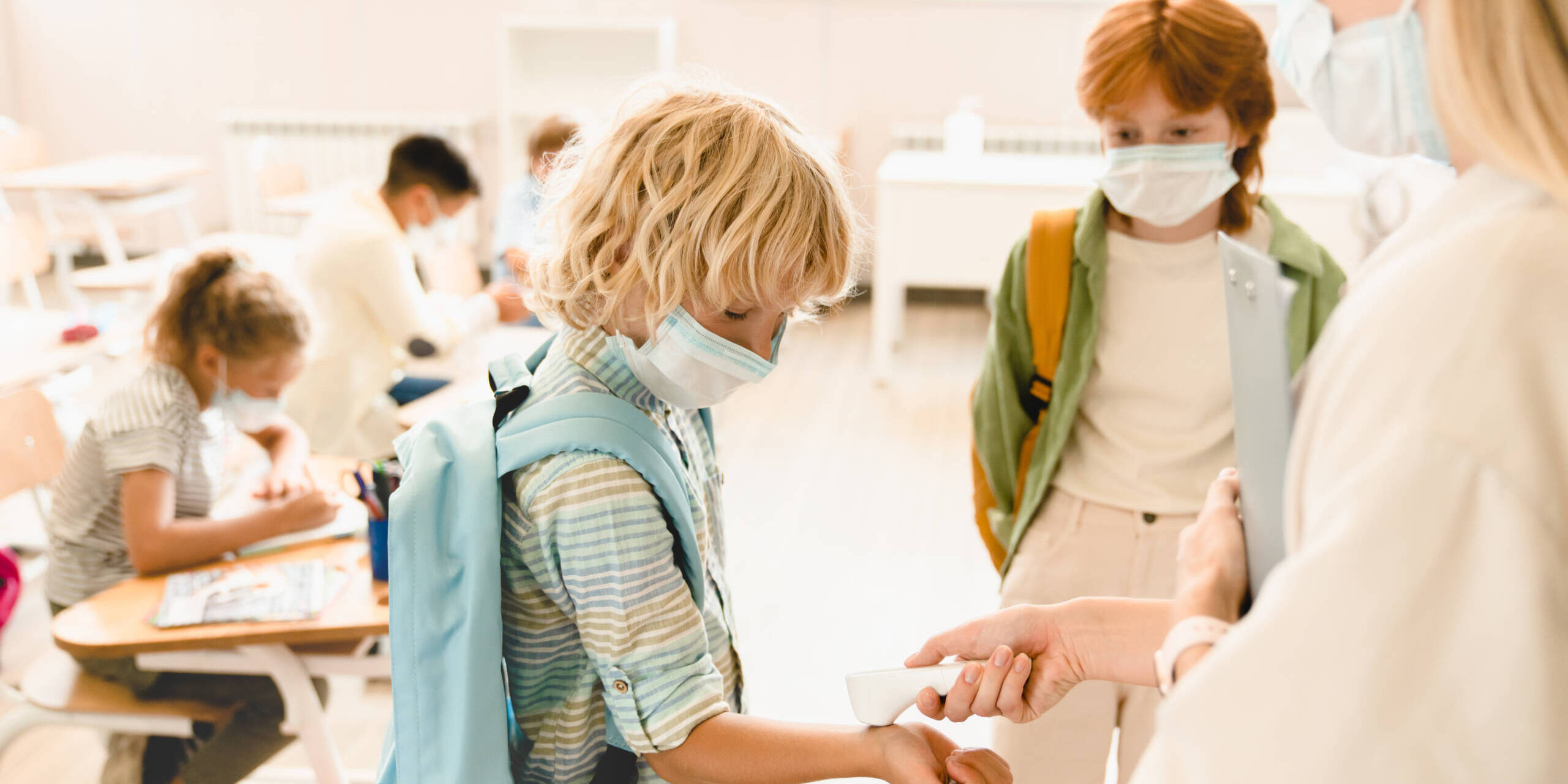 Teacher measuring temperature her students classmates schoolchildren before lesson wearing protective medicine face masks against coronavirus Covid19 due to lockdown restrictions. kids at the school nurse